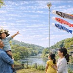 A Japanese family enjoying Children's Day with traditional koinobori carp streamers flying from a pole beside a river in spring